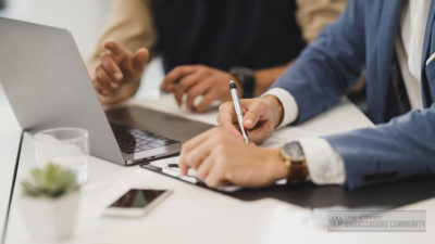 two individuals' hands with computer and notebook